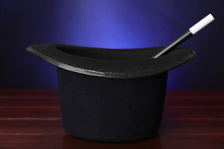 Black top hat and wand on wooden table against color background, closeup. Magician equipmentの写真素材