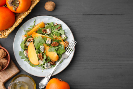 Tasty salad with persimmon, blue cheese and walnuts served on gray wooden table, flat lay. Space for textの写真素材