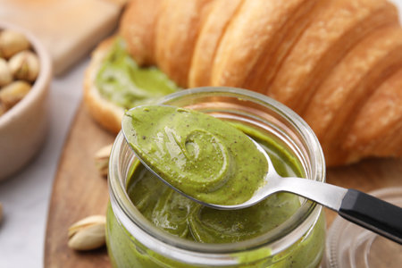Tasty pistachio cream in jar and spoon, closeup