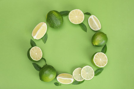 Frame of fresh limes and leaves on light green background, flat lay. Space for text