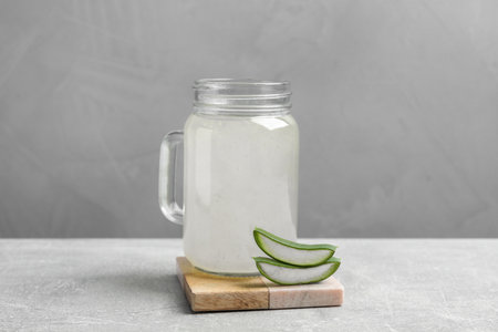 Tasty aloe juice in mason jar and cut fresh leaves on light gray tableの写真素材