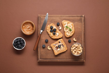 Toasts with tasty nut butter, blueberries, banana slices and cashews on brown table, flat layの写真素材