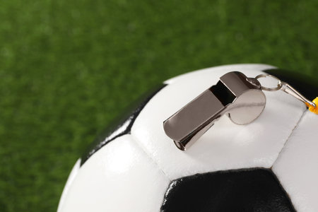 Football referee equipment. Soccer ball and metal whistle on green grass, closeup with space for textの写真素材