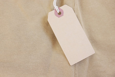 Cardboard tag on beige garment, top view. Space for textの写真素材