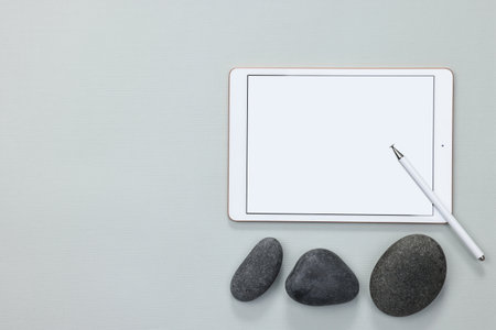 Modern tablet, stylus and pebbles on light gray background, flat lay. Space for textの写真素材
