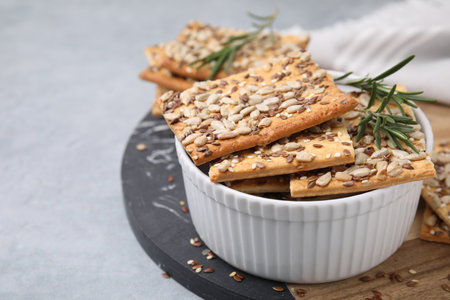 Cereal crackers with flax, sunflower, sesame seeds and rosemary in bowl on gray table, closeup. Space for textの写真素材