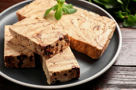 Pieces of tasty chocolate halva with mint on wooden table, closeup