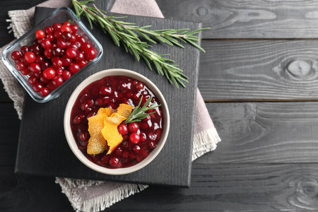 Fresh cranberry sauce, rosemary, orange peel and berries on black wooden table, top view. Space for textの写真素材
