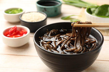 Eating delicious buckwheat noodle (soba) soup with chopsticks at white wooden table, closeupの写真素材
