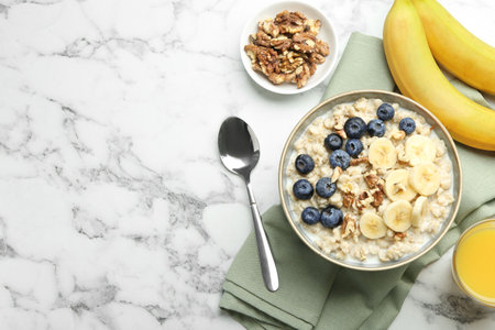 Tasty oatmeal with banana, blueberries, walnuts and milk served in bowl on white marble table, flat lay. Space for textの写真素材