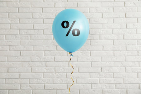 Discount offer. Light blue balloon with percent sign against white brick wall
