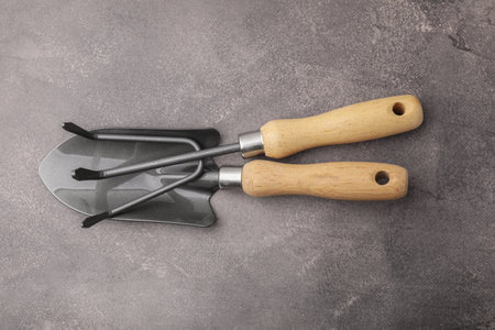 Gardening trowel and rake on brown textured table, top view