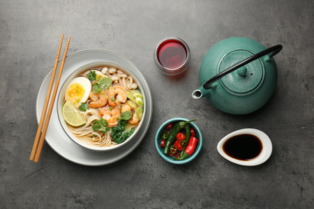Delicious ramen with shrimps and egg in bowl served on gray table, flat lay. Noodle soupの写真素材