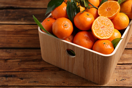Fresh tangerines with green leaves in crate on wooden table, closeupの写真素材
