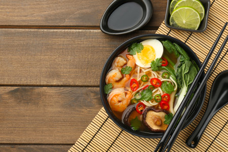 Delicious ramen with shrimps and egg in bowl served on wooden table, flat lay with space for text. Noodle soupの写真素材