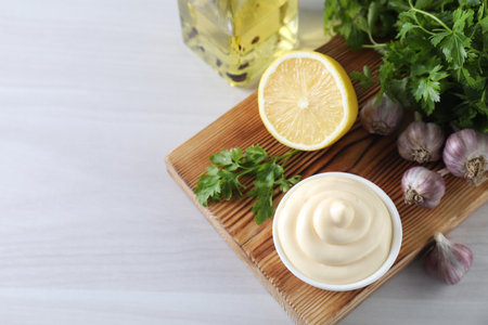 Tasty mayonnaise sauce in bowl, parsley, garlic and lemon on white wooden table, above view. Space for textの写真素材