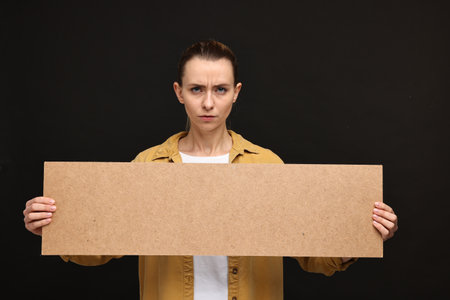 Angry woman holding blank cardboard banner on black background, space for textの写真素材