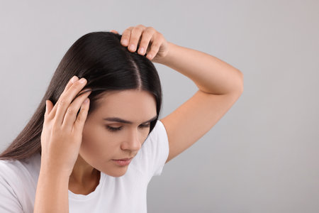 Woman examining her hair and scalp on gray background, closeup. Space for textの写真素材