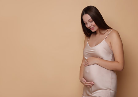 Beautiful pregnant woman in dress on beige background, space for text