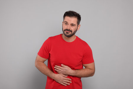 Man suffering from stomach pain on gray backgroundの写真素材