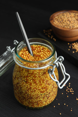 Whole grain mustard and spoon in jar on black wooden tableの写真素材