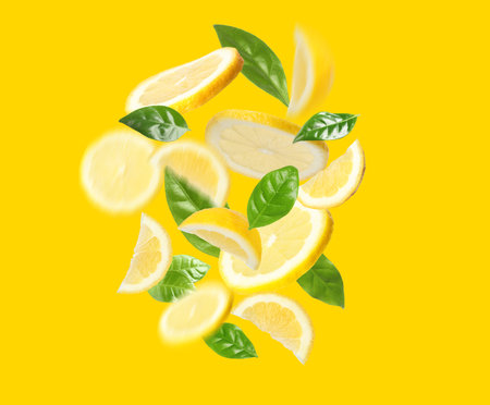 Fresh lemons and green leaves falling on golden backgroundの写真素材