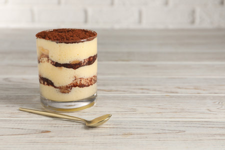 Delicious tiramisu in glass and spoon on light wooden table. Space for textの写真素材