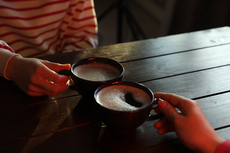 Women with cups of hot coffee at wooden table, closeupの写真素材
