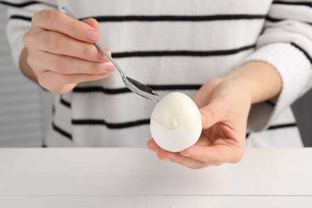 Woman eating boiled egg with spoon at white wooden table, closeupの写真素材
