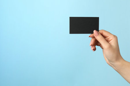Woman with blank black business card on light blue background, closeup. Mockup for designの写真素材