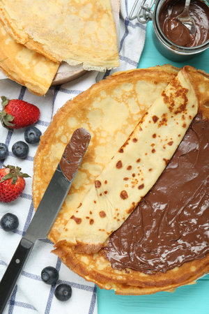 Tasty crepes with chocolate paste and berries served on turquoise wooden table, flat layの写真素材