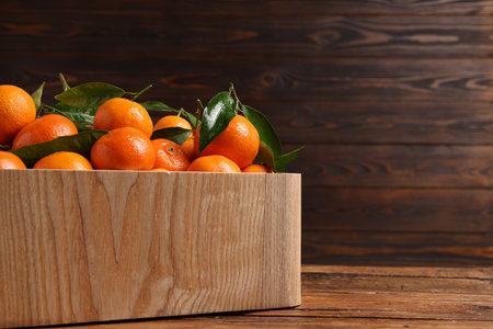 Fresh tangerines with green leaves in crate on wooden table, closeup. Space for textの写真素材