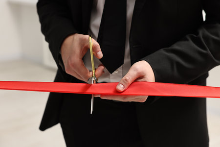Man cutting red ribbon with scissors on blurred background, closeupの写真素材