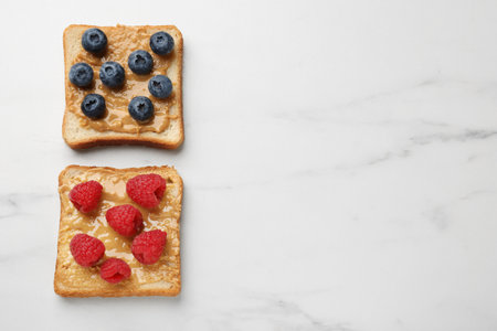 Delicious toasts with peanut butter, raspberries and blueberries on white marble table, flat lay. Space for textの写真素材