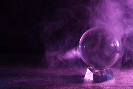 Crystal ball on table and smoke against dark background, space for text. Predictions of the futureの写真素材