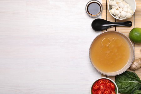 Cooking delicious ramen soup. Different ingredients and spoon on white wooden table, flat lay. Space...
