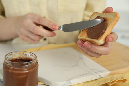 Woman spreading tasty nut butter onto toast at table, closeupの写真素材