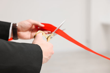 Woman cutting red ribbon with scissors indoors, closeupの写真素材