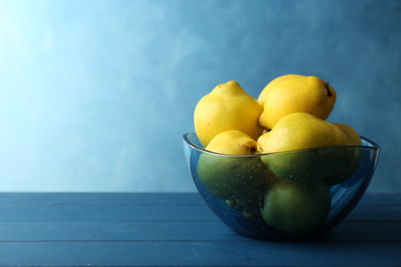 Tasty ripe quinces in bowl on blue wooden table, space for text