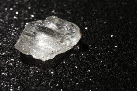 Beautiful rough diamond on dark shiny background, closeup. Space for text