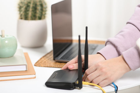 Woman connecting cable to WiFi router at table indoors, closeup