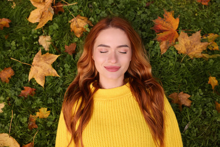 Beautiful woman lying on grass among autumn leaves, top view