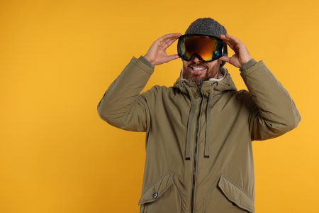 Winter sports. Happy man in ski suit and goggles on orange background, space for textの写真素材
