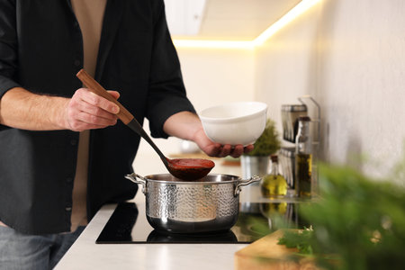 Man pouring delicious tomato soup into bowl in kitchen, closeupの写真素材