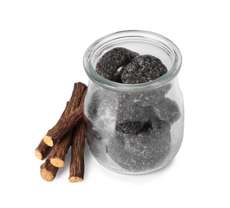 Glass jar of tasty candies and dried cut liquorice root isolated on whiteの写真素材