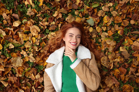 Smiling woman lying among autumn leaves outdoors, top viewの写真素材