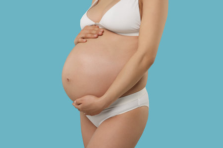 Pregnant woman in stylish comfortable underwear on light blue background, closeupの写真素材
