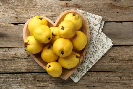 Tasty ripe quinces in heart shaped bowl on wooden table, top viewの写真素材
