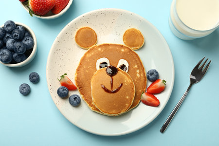 Creative serving for kids. Plate with cute bear made of pancakes and berries on light blue table, flat layの写真素材