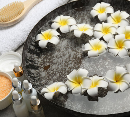 Bowl of water with flowers and different spa supplies on tableの写真素材